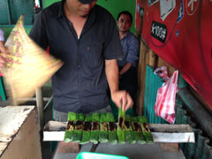 Man grilling otak-otak in front of a restaurant.